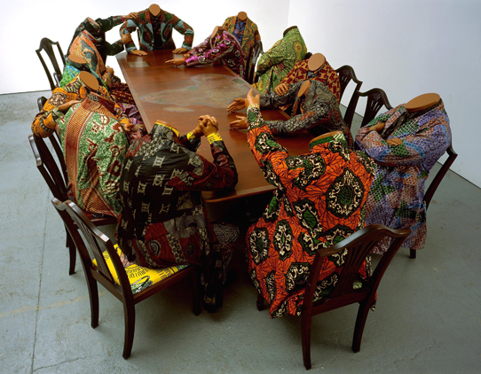 Yinka Shonibare MBE (b. United Kingdom, 1962). "Scramble for Africa" (2003). Fourteen life-size fiberglass mannequins, fourteen chairs, table, Dutch wax printed cotton, 52 x 192 x 110 in. The Pinnell Collection, Dallas. Image courtesy of the artist, Stephen Friedman Gallery, London, & James Cohan Gallery, New York. © the artist. Photo: Stephen White  