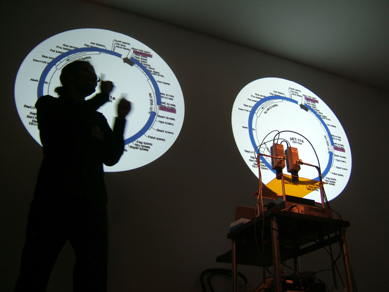Paul Vanouse, “Latent Figure Protocol,” Performance still: explaining DNA imaging process. ARS Electronica 2007, OK Center, Linz, Austria. Courtesy of the artist.