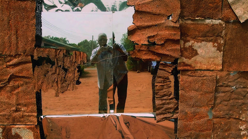El Anatsui taking a photograph of himself in the reflection of “Broken Bridge II” (2012) at his studio in Nsukka, Nigeria. Production still from the series Exclusive. © Art21, Inc. 2013. Image courtesy El Anatsui.