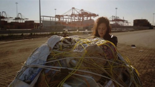 Artist Mary Mattingly pushing a sculpture of her personal belongings at the Port Newark Container Terminal, Newark, NJ, 2013. Production still from the "New York Close Up" film, "Mary Mattingly Owns Up". © Art21, Inc. 2013.