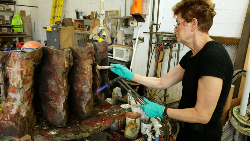 Artist Ursula von Rydingsvard applying a patina to a section of her bronze sculpture Ona. Production still from the series Exclusive. © Art21, Inc. 2013. Cinematography by Ian Forster